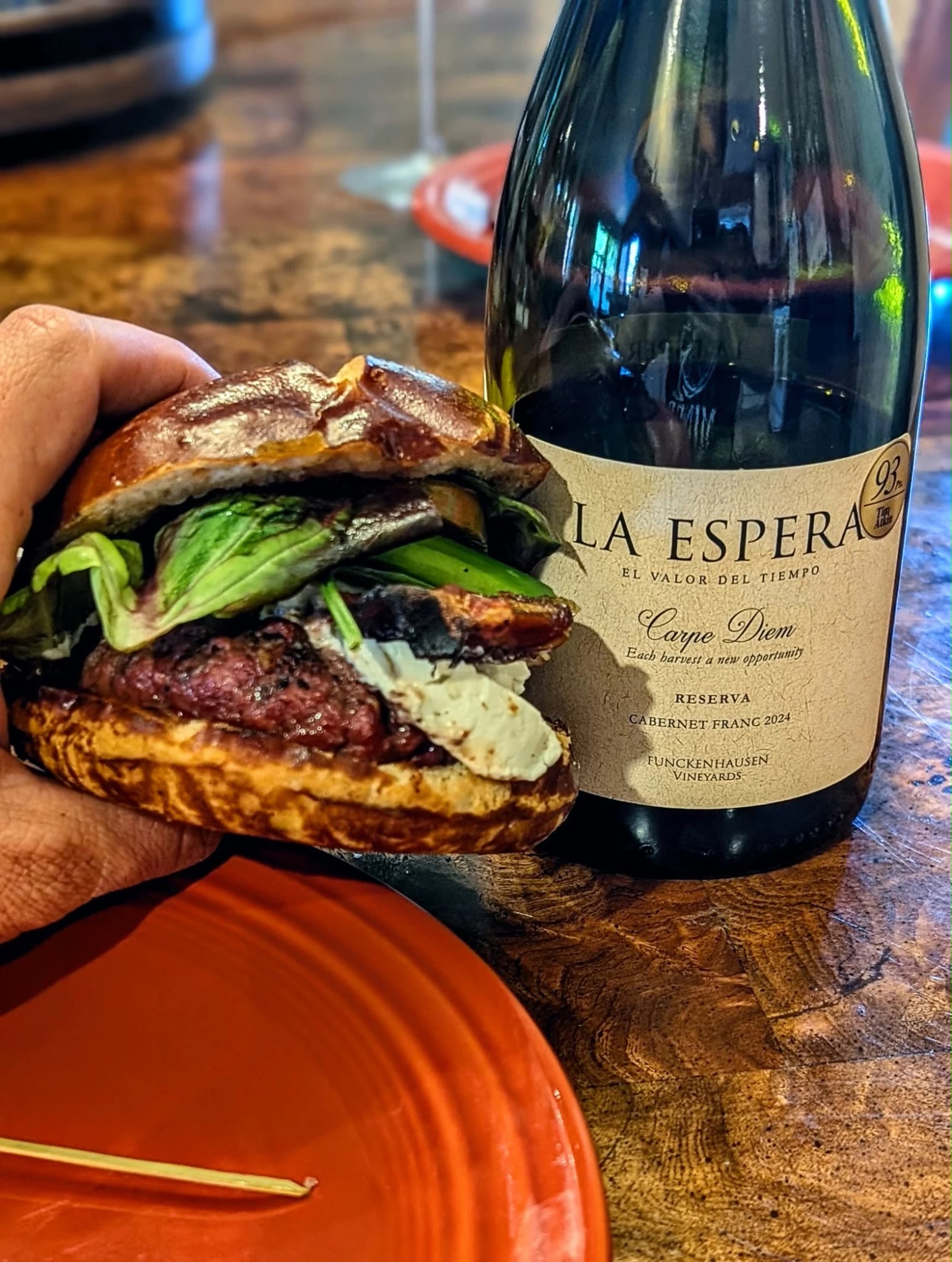 The Date Night Burger I made, on a pretzel bun with goat cheese and greens, next to a bottle of red